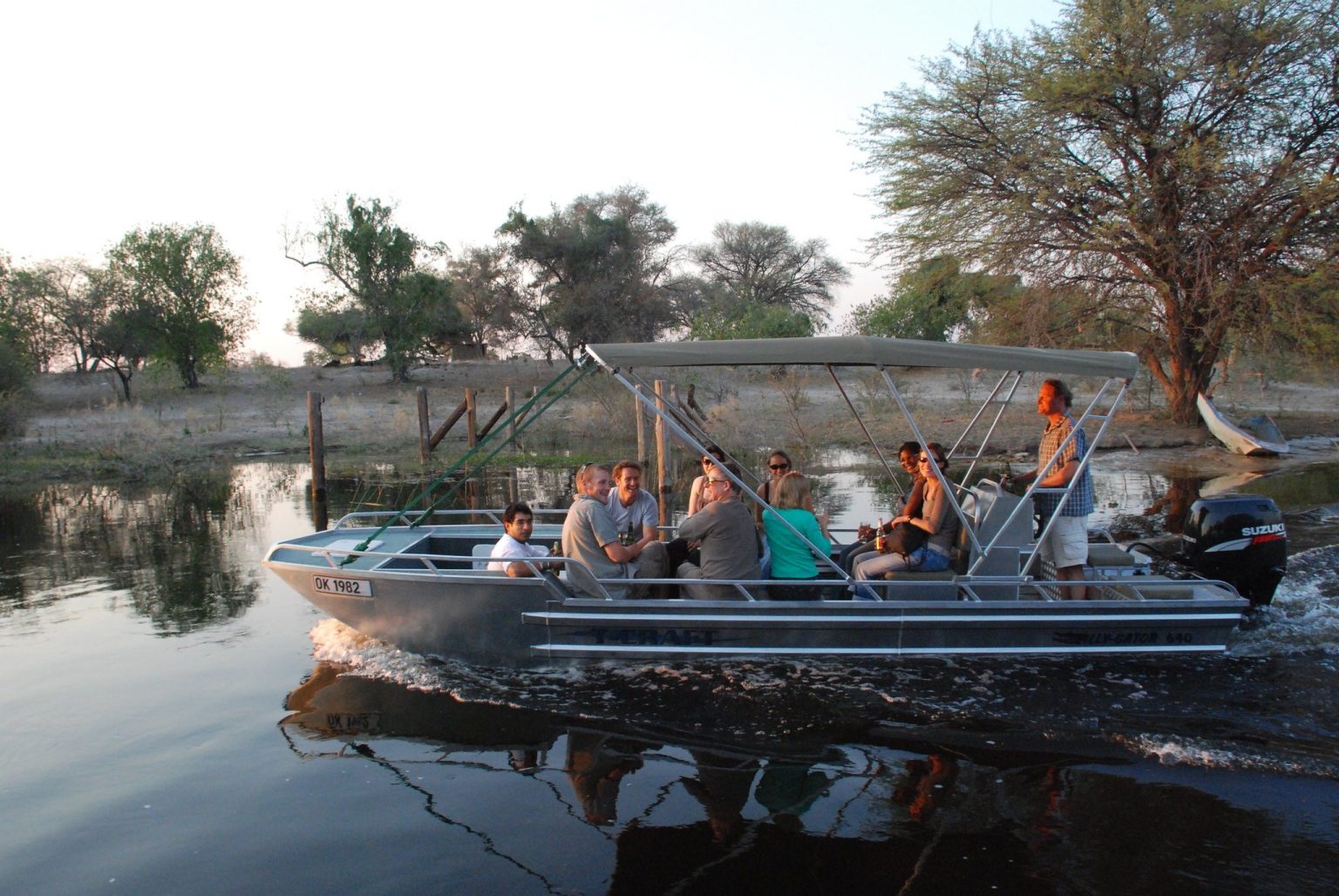 Guests on a small canopied boat cruising a calm river channel in Botswana