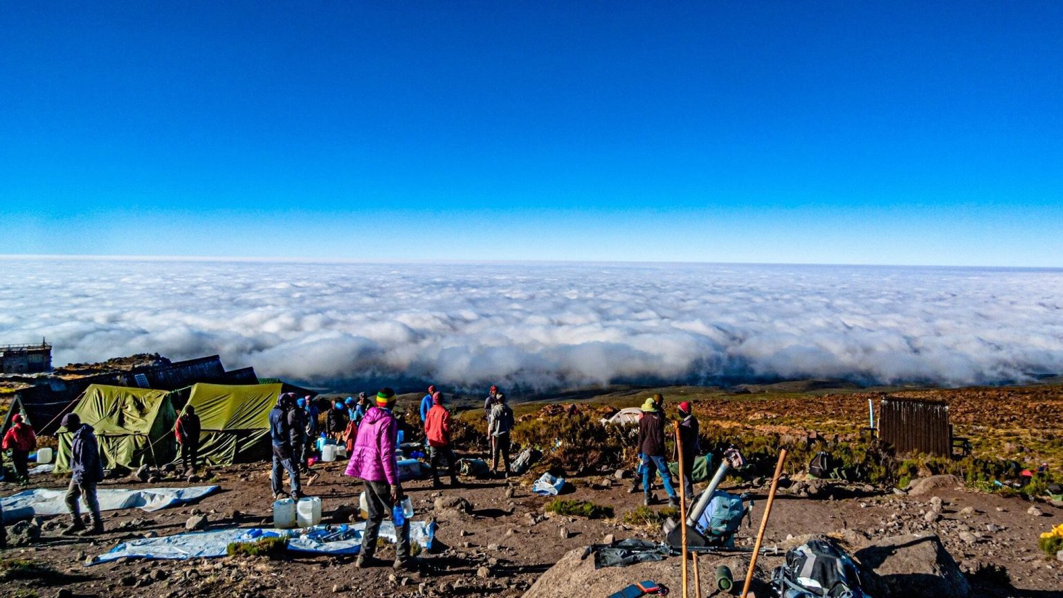 Trekkers and porters among the tents of a Kilimanjaro camp high above a sea of cloud