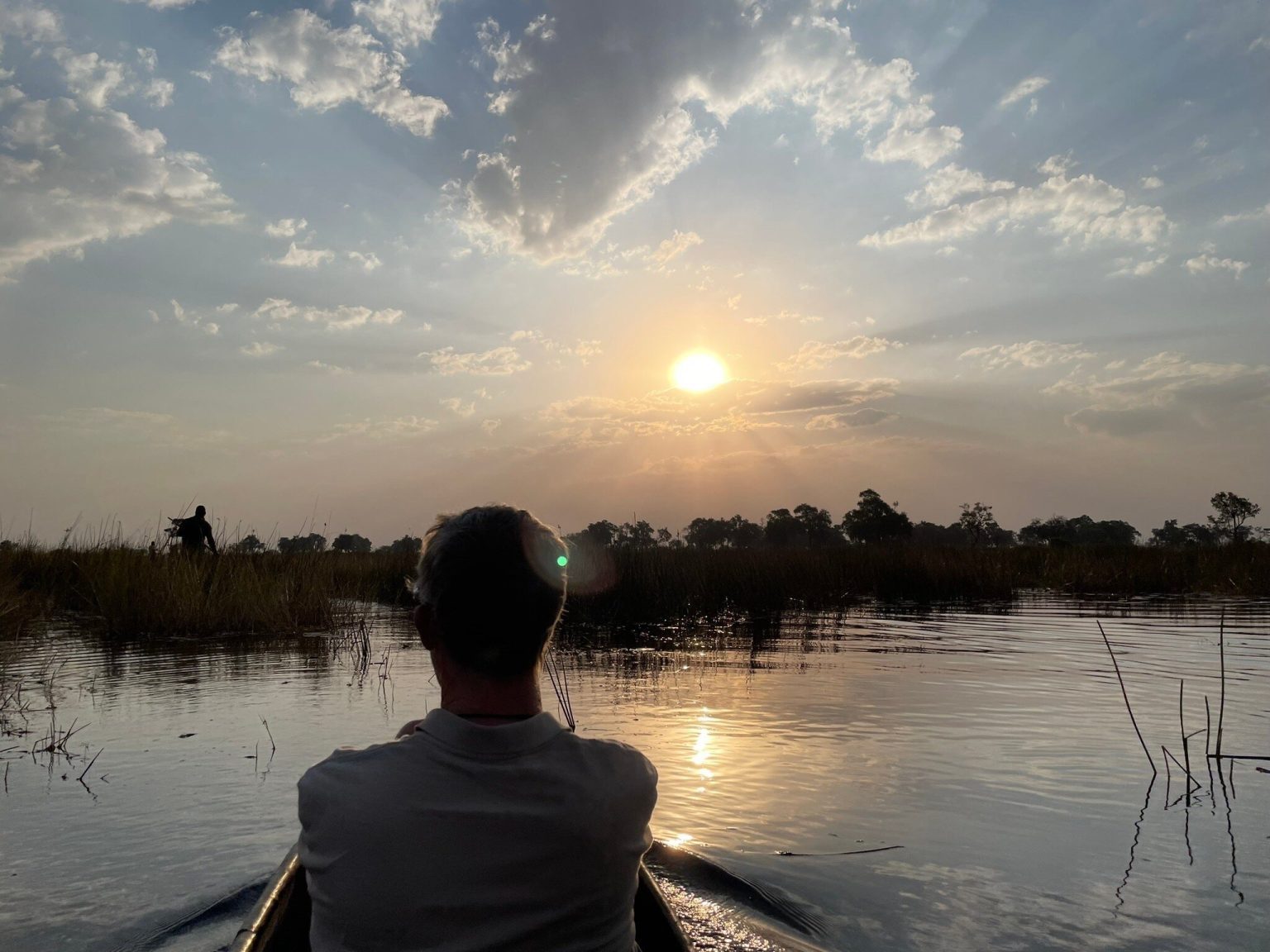 Guest in a mokoro canoe facing the setting sun over the Okavango Delta