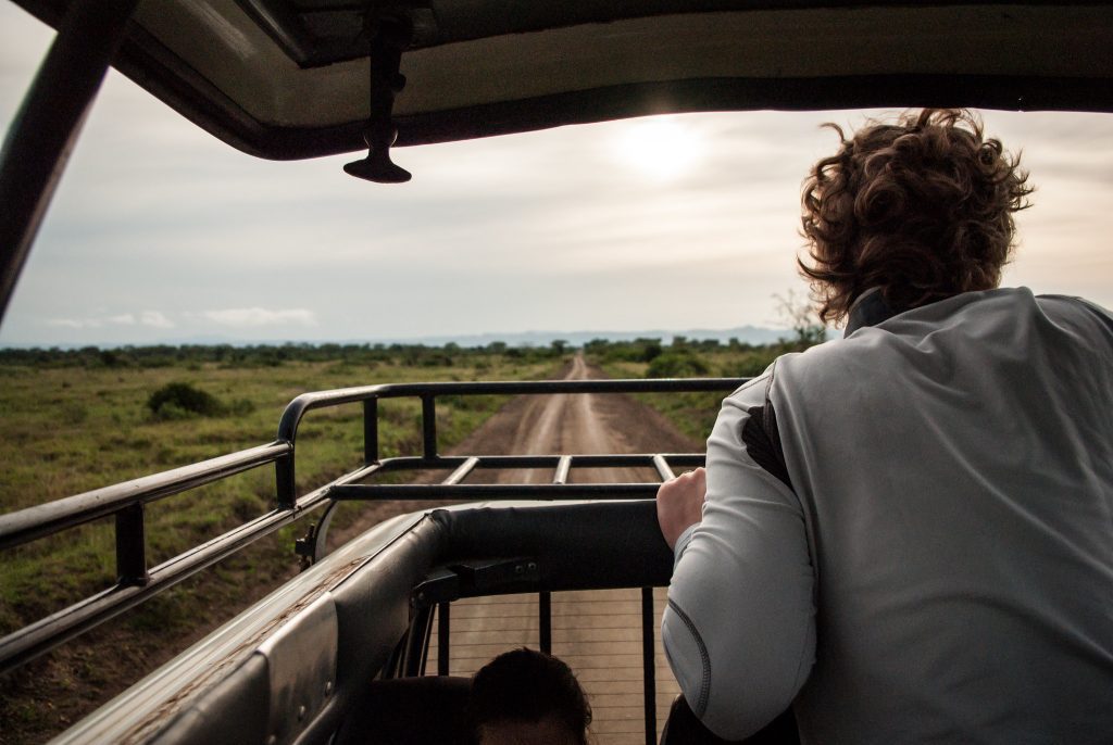 Traveller standing in the open roof of a safari vehicle on a dusty track