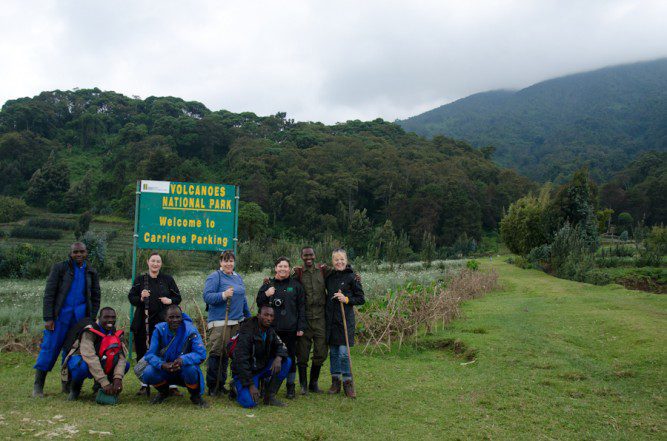 Gorilla trekkers with rangers and porters at the Volcanoes National Park sign in Rwanda