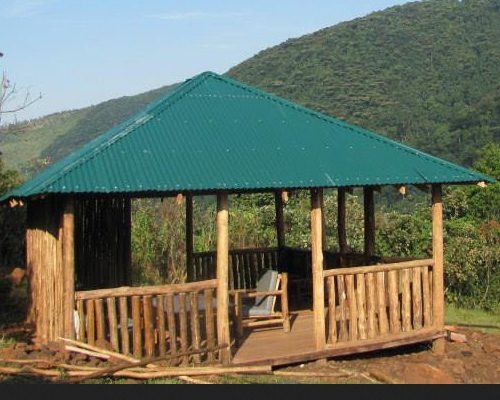 An open wooden shelter with a green roof at the Gorilla Conservation Camp above Buhoma
