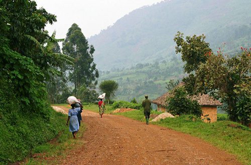 Villagers walking along a red dirt road through hills in rural Uganda