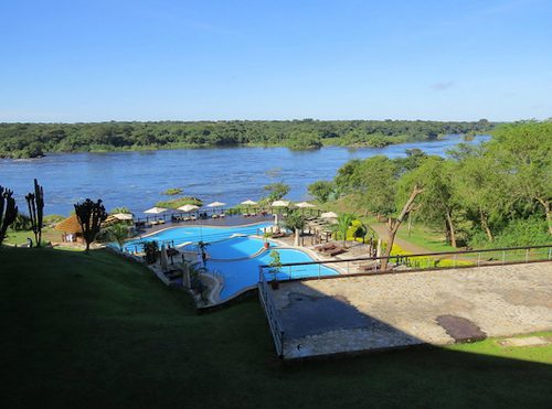 A lodge swimming pool with sun umbrellas above the wide Victoria Nile in Murchison Falls National Park