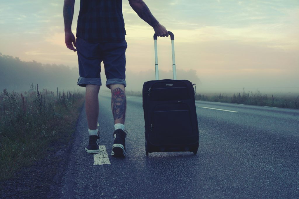 Traveller pulling a black wheeled carry on suitcase along an empty road at dawn