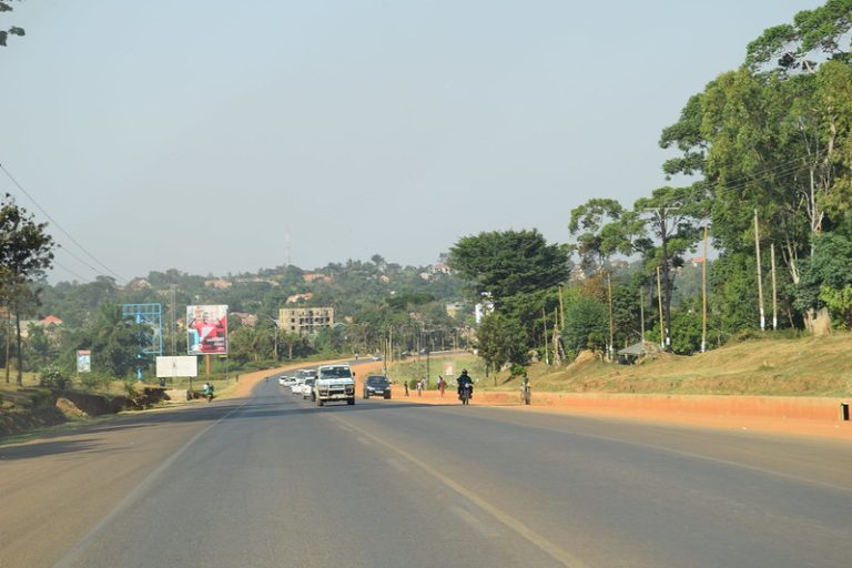 Traffic on the tarmac road between Entebbe and Kampala in Uganda with trees and red earth verges