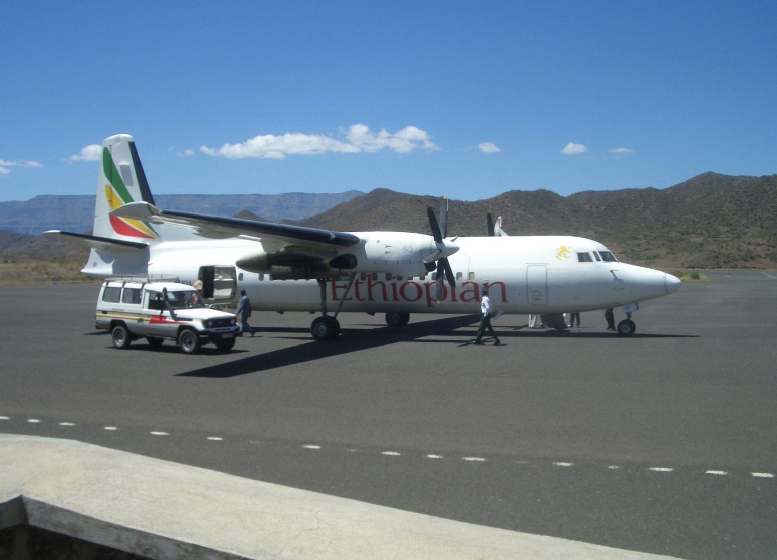 An Ethiopian Airlines turboprop parked on the apron at Lalibela airport with a vehicle alongside