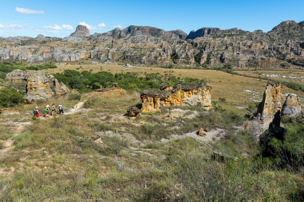 Hikers on a grassy trail below eroded sandstone cliffs on Madagascar's RN7 route