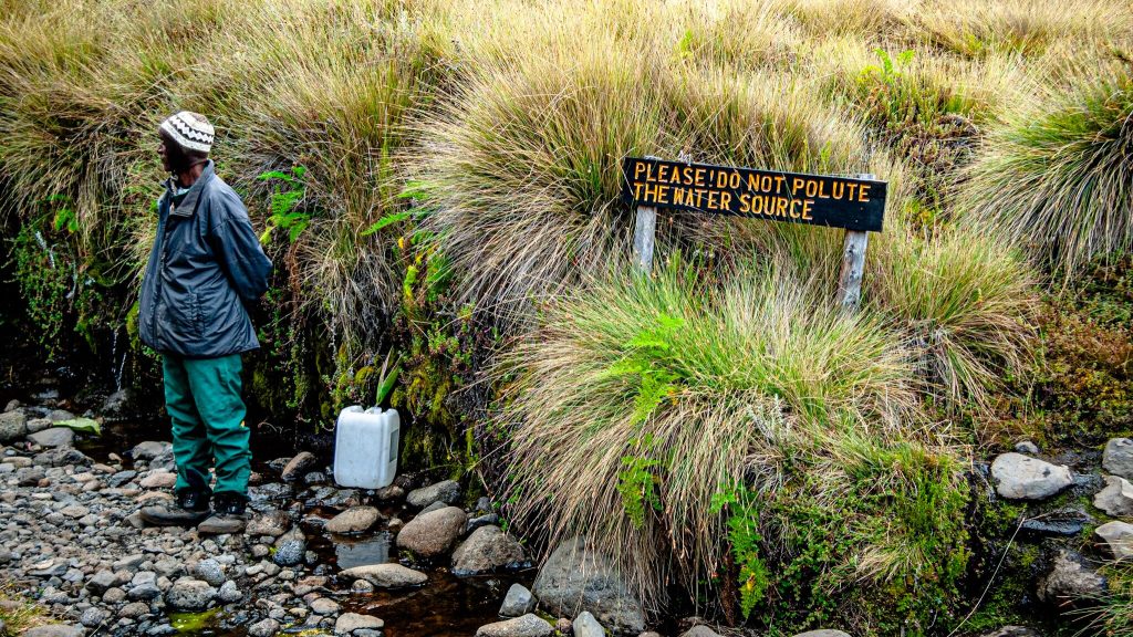 Porter collecting water in a jerrycan at a stream on Kilimanjaro beside a do not pollute sign