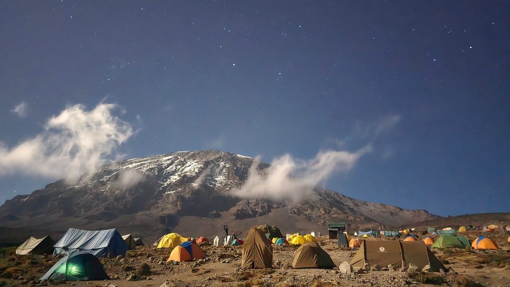 Tent camp under a starry sky below the snow streaked summit of Kilimanjaro