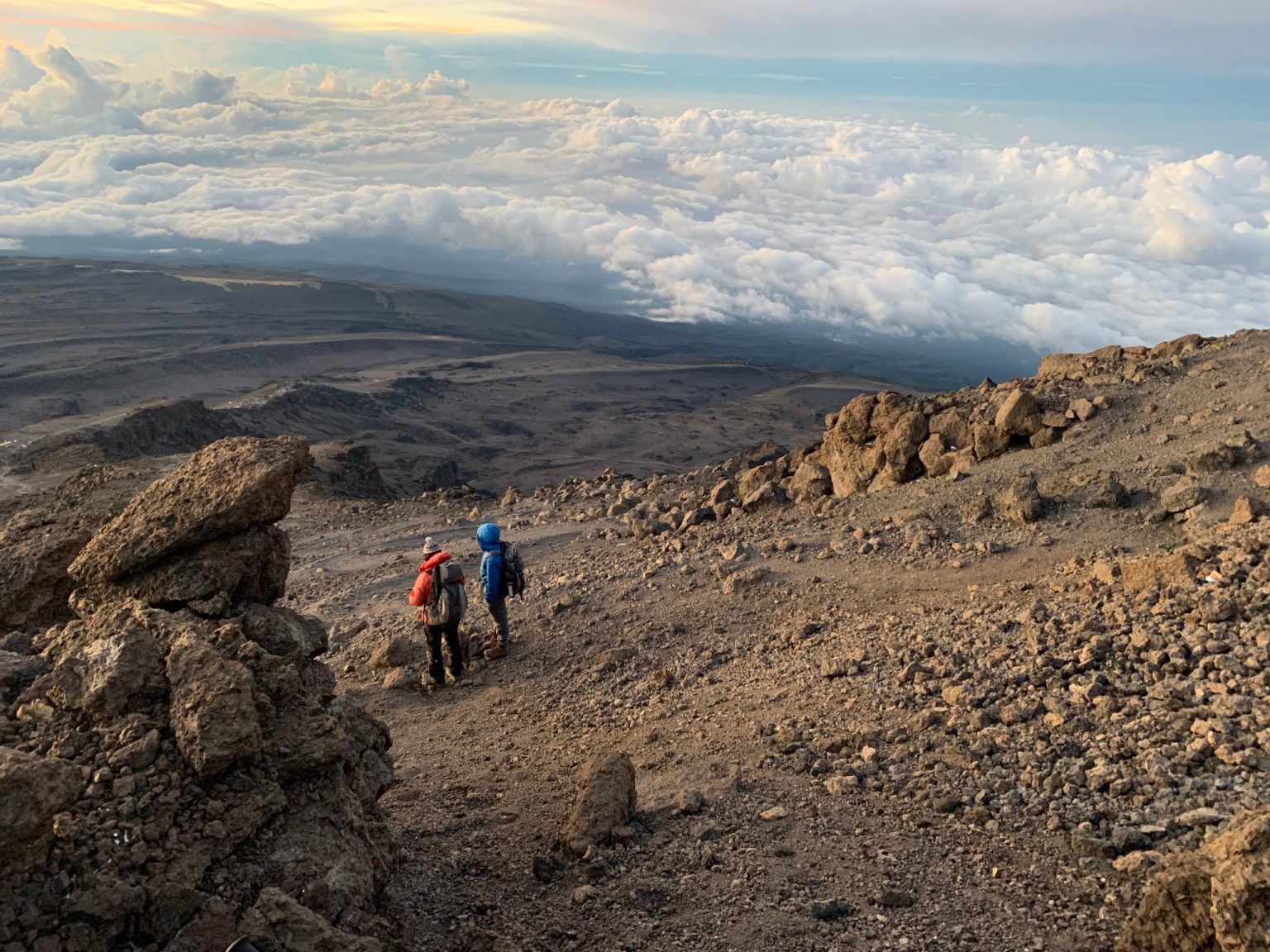 Two trekkers crossing bare alpine desert scree high on Kilimanjaro above a sea of cloud