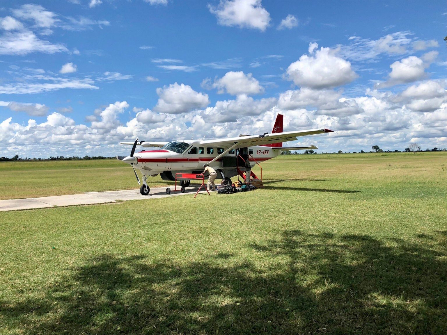 Single engine safari bush plane being loaded with bags on a grass airstrip