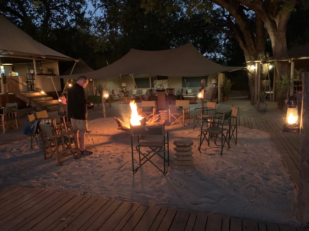Campfire and lanterns in front of the tents of a safari camp at dusk