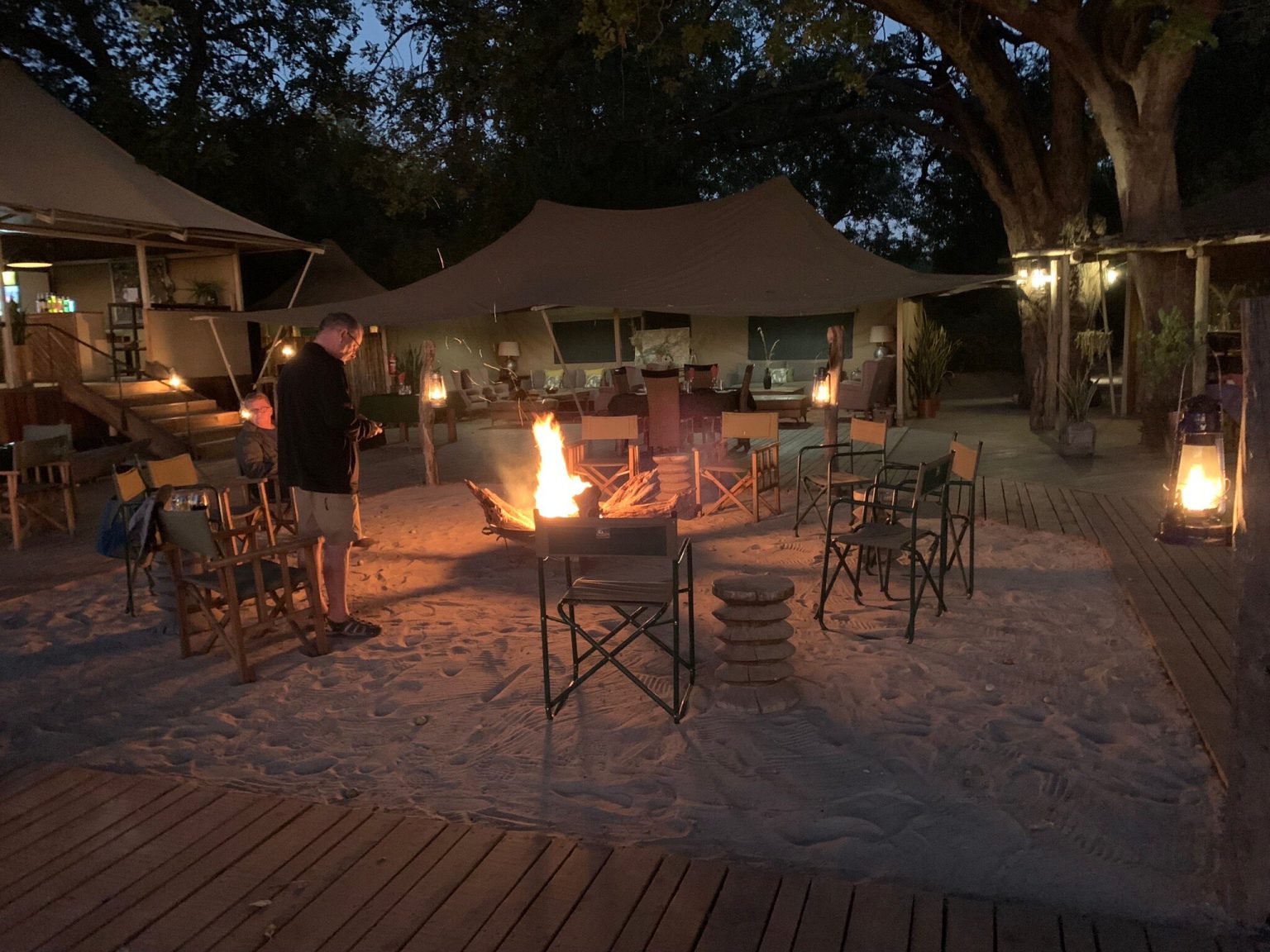 Campfire and lanterns in front of the tents of a safari camp at dusk