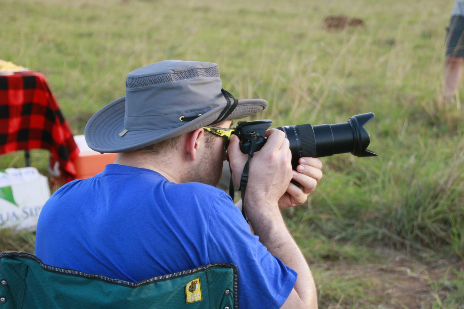 Safari guest in a brimmed hat photographing wildlife with a camera and telephoto zoom lens