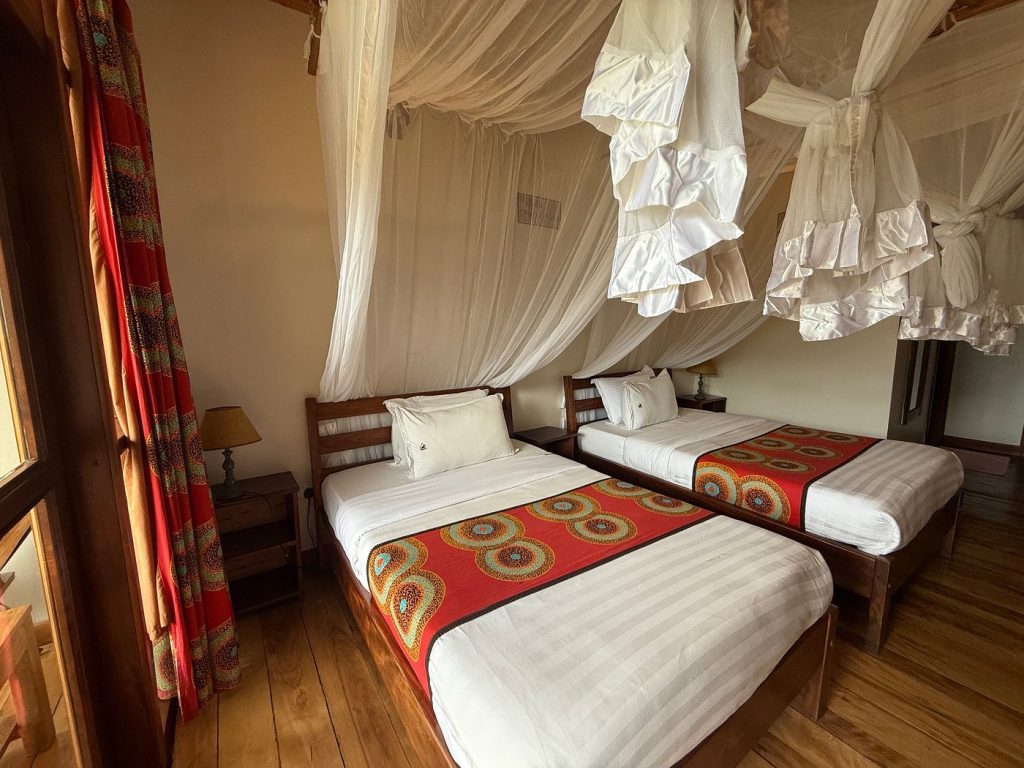 Twin beds under white mosquito nets in a lodge room near Bwindi