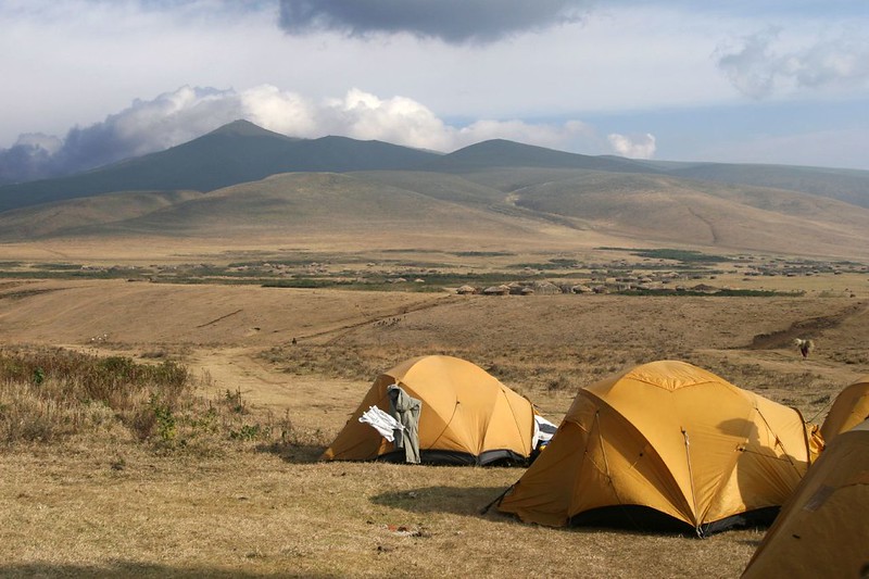 Yellow dome tents pitched on grassland in the Ngorongoro highlands with Maasai homesteads and hills behind